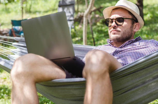 istock Man in hat lying in hammock and looking at his laptop. 1404050833