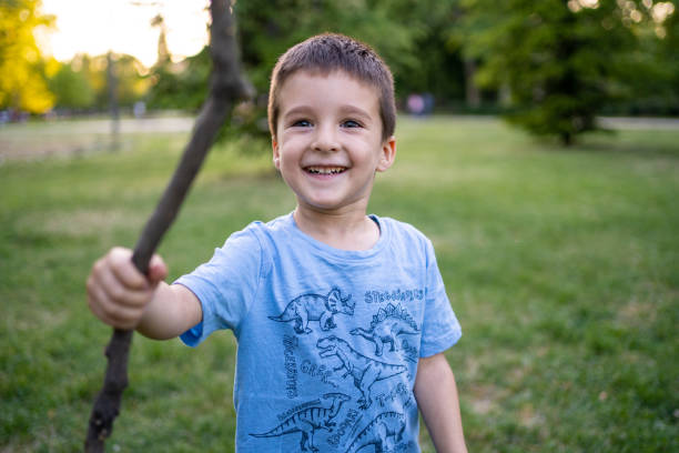 Portrait of a cute kid boy in the tree cavity on a sunny day. Curious child looking out of a tree hollow while hiding in the park. Playing and exploring boy outdoors.