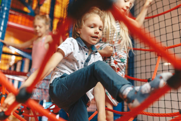 excited kids playing together on net ropes. happy group of siblings playing together on indoor playground. cute school kids playing on the colorful playground at shopping mall - child jungle gym playground laughing imagens e fotografias de stock