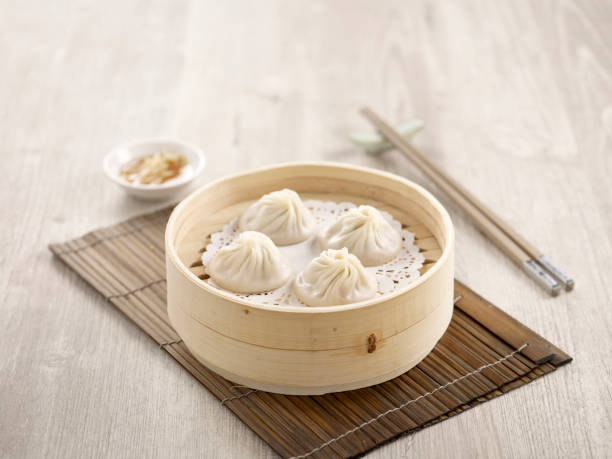 Steamed Xiao Long Bao with chopsticks served in a dish isolated on mat side view on grey background