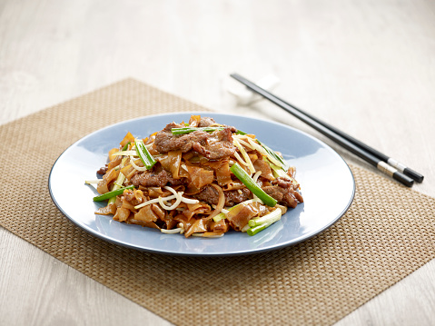 Stir-fried Hor Fun with Sliced Beef with chopsticks served in a dish isolated on mat side view on grey background