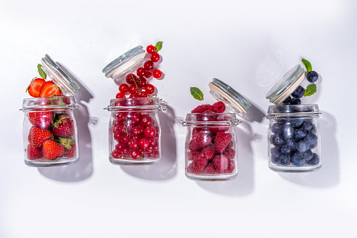 Fruit an berry jam preservation, summer canned food for winter, summer harvest, healthy diet take away snack concept. Raspberry, blueberry, strawberry, cherry in glass jars for conservation