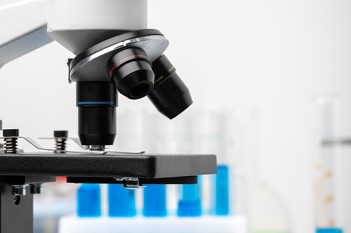 Microscope and colored test tubes on table in laboratory, close up