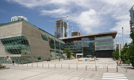 Surrey, Canada - June 17, 2022: The Surrey Libraries - City Centre Branch stands to the left on Surrey Civic Plaza. Surrey City Hall to the right was designed by Moriyama & Teshima Architects of Toronto. Background shows residential buildings under construction in the downtown district. Spring midday with light clouds over Metro Vancouver.