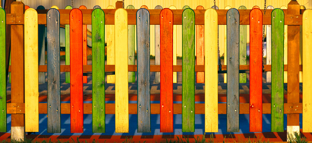 Multicolored wooden fence surrounding a children playground at dusk, close-up front view. Galicia, Spain.