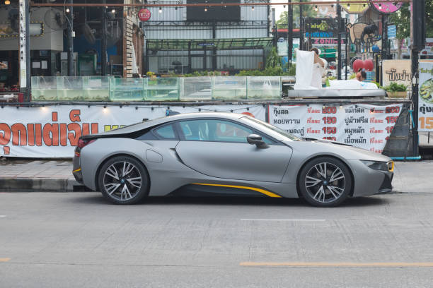 Side view of gray colored BMW i8 parked in front of a restaurant in street Wanghin Road in Bangkok. At open restaurant are a few people at right side
