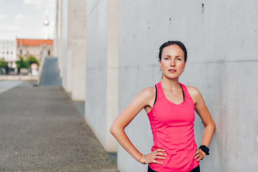 portrait of young sportswoman wearing pink shirt in front of concrete wall