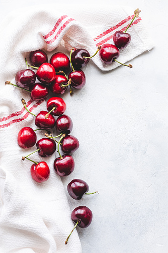 Top view of a bunch of cherries with a kitchen rag on a white wooden table, with copy space
