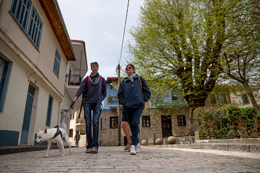 Mature Couple With a Pet Dog Walking Around A Village on Springtime Discovery Vacation In Greece