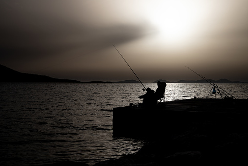Silhouette of two Fisherman Fishing At Sunset in Ionian Sea from a Jetty in Greece