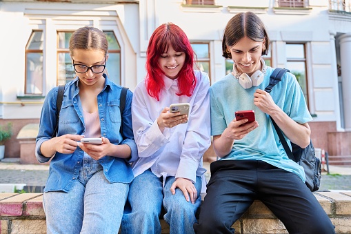 Teenage friends together outdoor having fun using smartphones on city street. Technology mobile apps, lifestyle, vacation leisure, urban style, youth concept