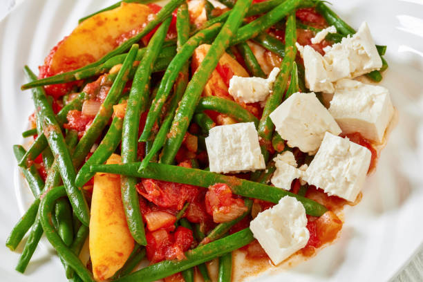 fasolakia lathera, green beans, onion and potatoes stewed in tomato, herbs and olive oil on white plate served with feta cheese, greek cuisine, close-up