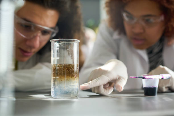 Student pointing at glass containing chemical dissolver during experiment stock photo