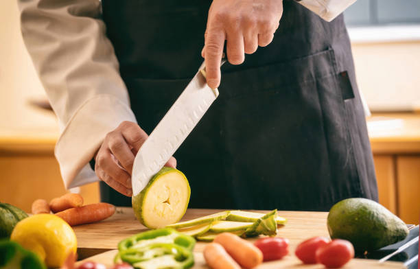 Chef cut zucchini with a knife on a chopping board, close up. Fresh vegetable on kitchen table.
