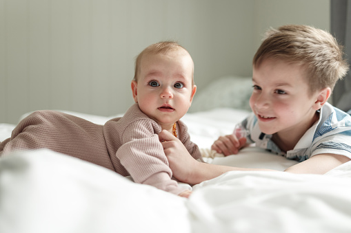 Portrait of six months crawling baby on fluffy white rug, happy smiling adorable sweet little girl kid lying on bed in bedroom, childhood and baby care concept