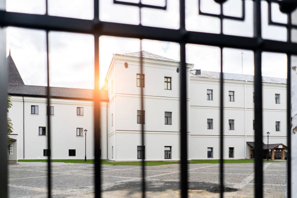 Big white Building and low sun shining seen through the gate. View through fence