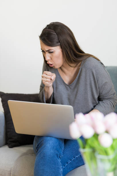 istock Young woman coughing while using her laptop 1404076886