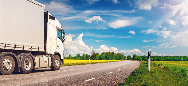 Truck moving on the asphalt country highway in sunny day in spring. Concept of logistic and freight transportation.