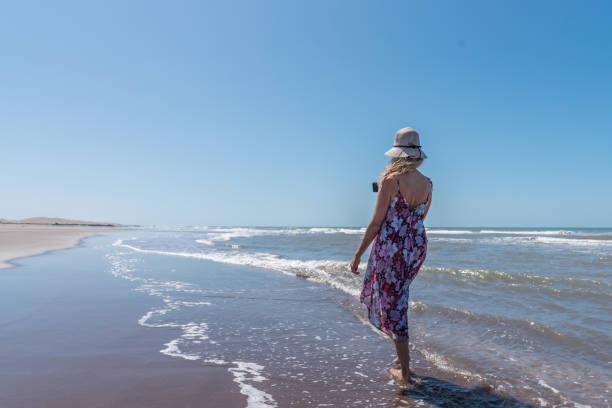 istock Woman strolling barefoot along the beach recording with a mobile 1404078917