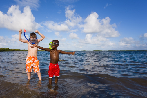 Two small boys playing with snorkel gear on a beach - one African American one Caucasian. John Pennecamp Park, Florida Keys.