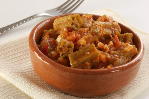 A recipe of okras (gumbos, Bamias) in mediterraneal tomato's sauce with garlic, onion, chili, etc. with fork and napkin