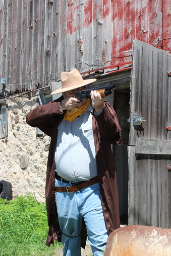 Man in victorian cowboy clothing with revolver in holster standing on prairie area.