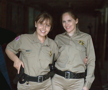 two female uniformed deputy sheriffs setting up caution tape at a scene, with rifles and shotguns