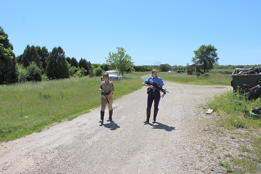 two white female motorcycle police officers setting up caution tape at a crime scene in full uniform with rifle and shotgun conducting surveillance duties