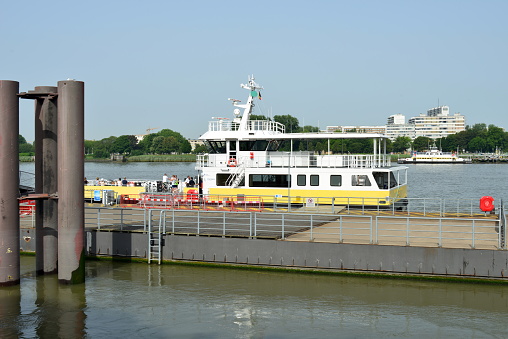 Antwerp city, Province Antwerp , Belgium - June 18, 2022: yellow-white moored tour boat on the quay. White people some with bicycle waiting departure ship to cross the river