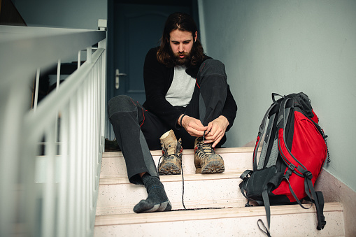 One man, young male hiker sitting on steps and putting on hiking boots before leaving on adventure.