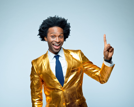 Portrait of businessman laughing while pointing in golden suit against blue background