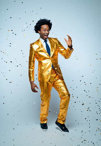 Cheerful businessman in golden suit dancing amidst confetti against blue background