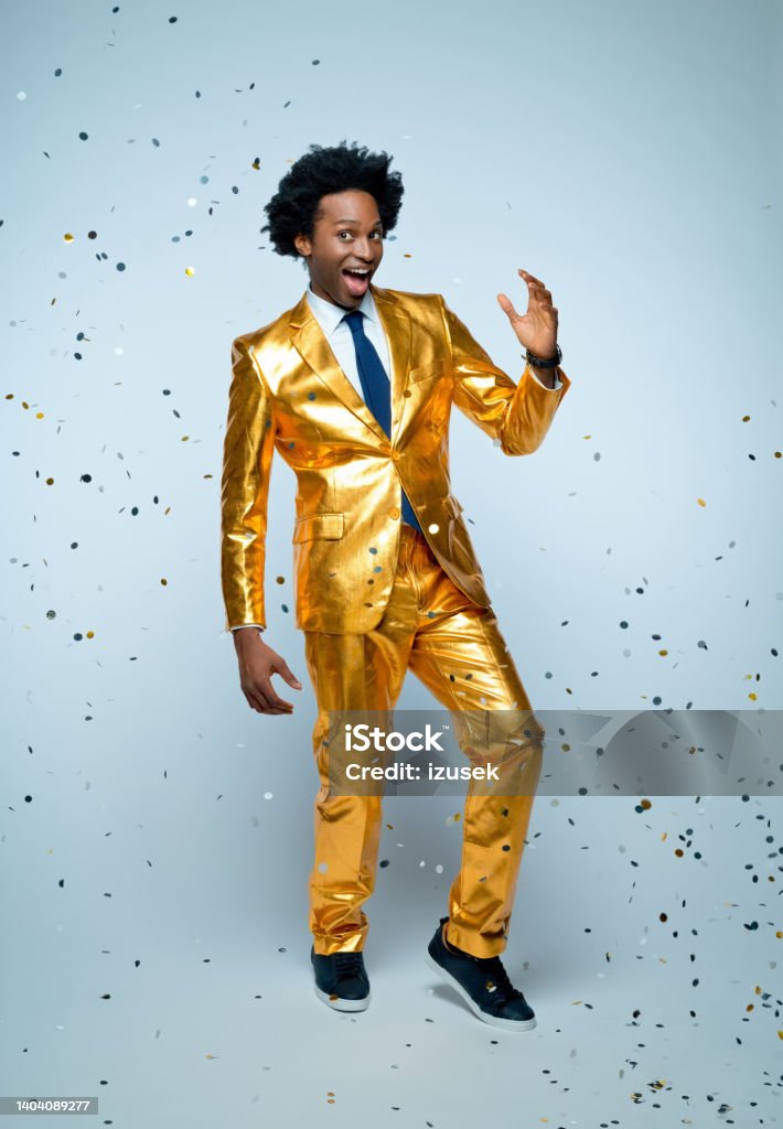 Man dancing amidst confetti Cheerful businessman in golden suit dancing amidst confetti against blue background Confetti Stock Photo