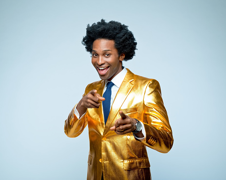 Portrait of happy businessman in golden blazer pointing while standing against blue background