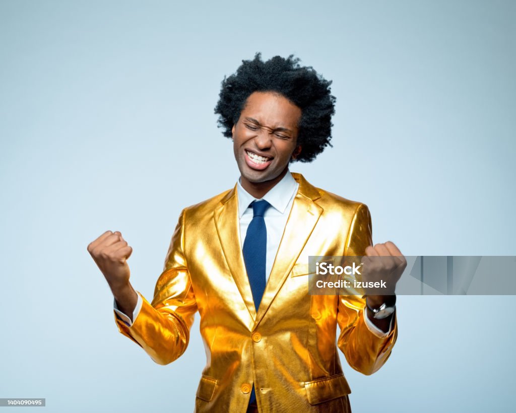 Happy businessman clenching fists Successful businessman clenching fists against blue background Gold Colored Stock Photo