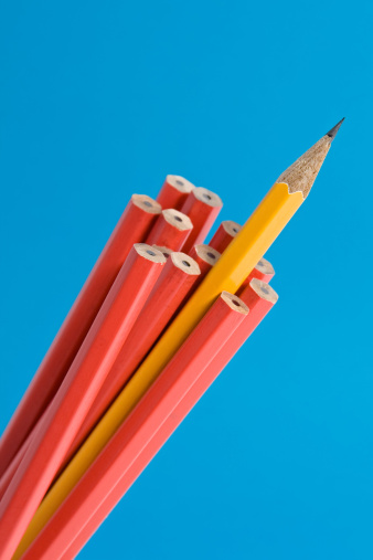 Close up shot of a sharp yellow pencil amongst unsharpened red pencils. Narrow depth of field, shot against a blue background.