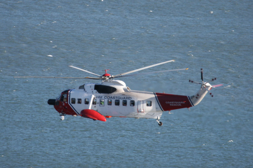 Coastguard helicopter hovering above the sea, viewed from cliff-top perspective