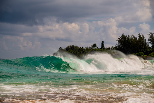 A wave crashes on a beach on the shore of the Pacific Ocean on the island of Kauai in Hawaii on a windy day.