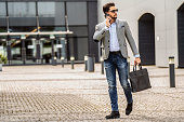 Handsome businessman walking on the street, talking via mobile phone. Fashionable style. Male model.
