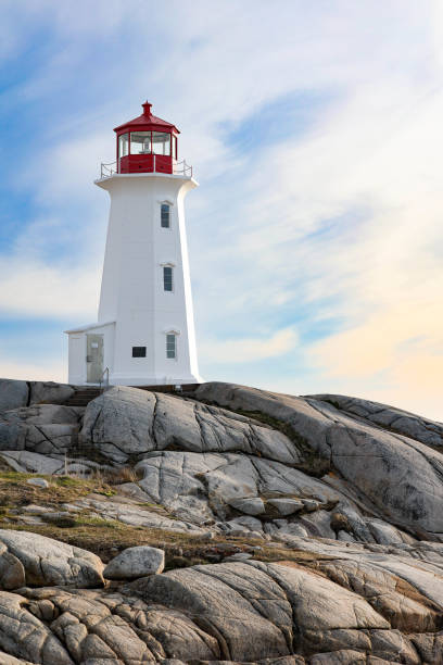 Lighthouse Sitting on Rocks with Clouds in the Sky Peggy’s cove lighthouse in Nova Scotia sitting on top of rocks with sky behind. Blue and orange sky with clouds allie stock pictures, royalty-free photos & images
