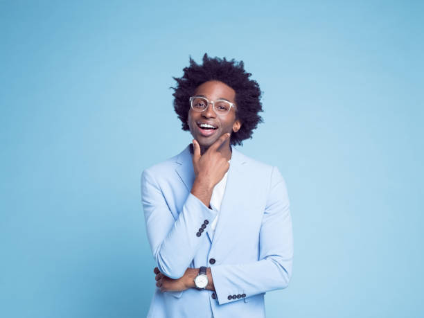 Happy businessman with hand on chin Portrait of happy businessman with hand on chin against blue background business person one man only blue standing stock pictures, royalty-free photos & images