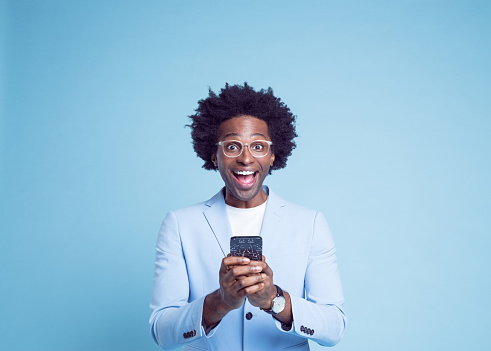 Portrait of cheerful businessman with smart phone against blue background