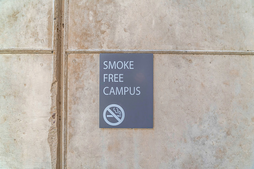 Smoke Free Campus sign on exterior wall of school building in San Diego CA. A no smoking icon can also be seen on the gray warning plate.