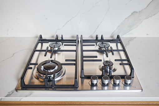 Modern hob gas or gas stove made of stainless steel using natural gas or propane for cooking products on light stoneware countertop in kitchen interior, with copyspace.