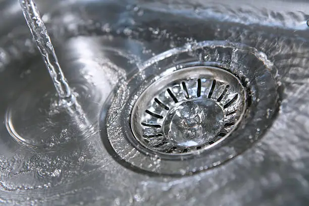 Closeup of fresh cold water running down the drain of a stainless steel kitchen sink