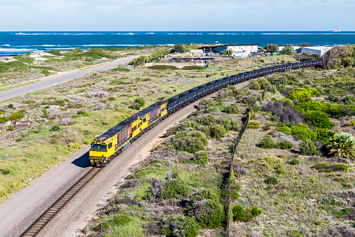 Nature and Industry: aerial view empty iron ore train curving through sand dunes with coast, ocean and large ship in background. ID & logos edited