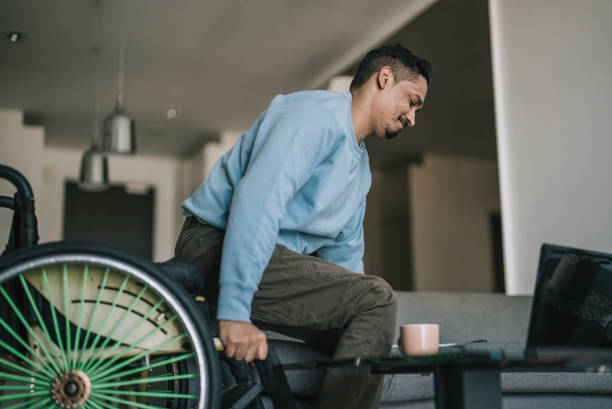 Asian indian with disability getting up from wheelchair and sitting on sofa stock photo