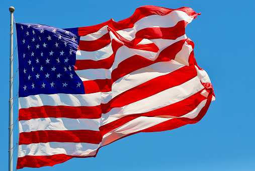 Close-up of a U.S. flag waving in a brusk wind against a clear blue sky.