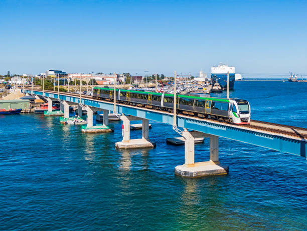Aerial view modern electric commuter train crossing river bridge with port activity in background