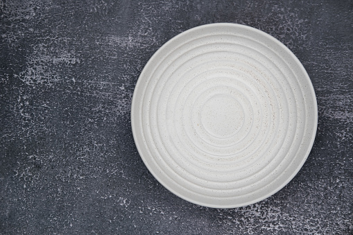 Empty white ceramic plate with rough texture, isolated on white background with clipping path, Side view